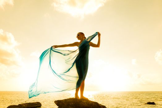 Freedom and beauty concept. Beautiful girl with blue scarf standing on the Rock. Flying. Free. Vacation