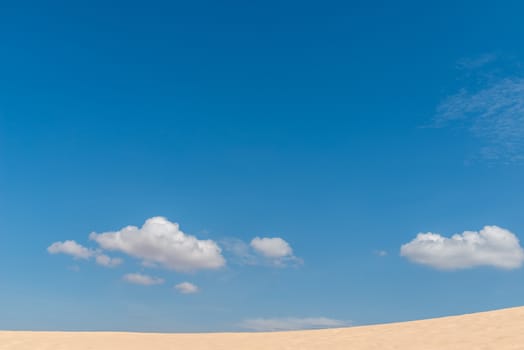 Desert sand dunes landscape with deep blue sky and clouds