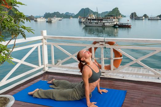 Young woman practicing yoga on the upper deck of ship. Morning time just after sunrise