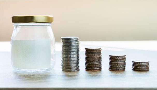 Money savings concepts. Put coins in glass bottles with paper label to spend on expenses such as savings, tourism, investment, emergency, retirement on wooden table with blur background