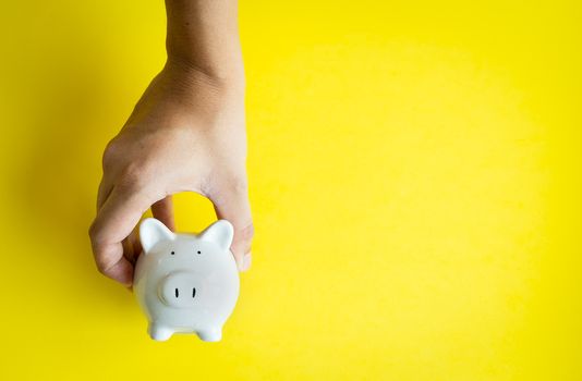 Money savings concepts. The piggy bank in hand is giving for savings, tourism, investment, emergency, retirement on yellow background and copy space