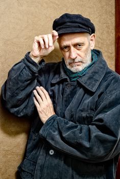 Portrait of a mature man with a white beard adjusting his cap on the head. He could be a sailor, a worker, a docker, or even a gangster or a thug. He has a penetrating gaze.