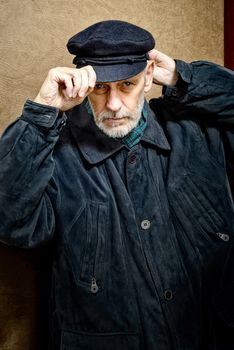 Portrait of a mature man with a white beard adjusting his cap on the head. He could be a sailor, a worker, a docker, or even a gangster or a thug. He has a penetrating gaze.