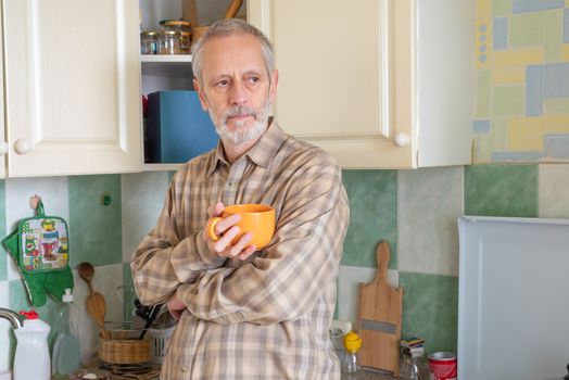 Mature man drinking his coffee in an orange cup, at morning in kitchen