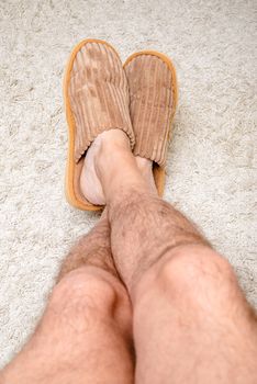 A man with hairy legs is wearing warm slippers and relaxing with the feet on a wool carpet