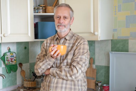 Mature man drinking his coffee in an orange cup, at morning in kitchen