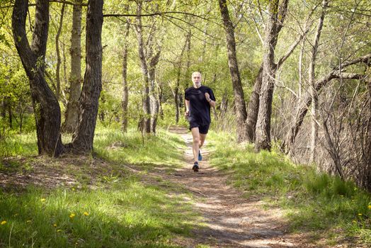 A senior man dressed in black is running in the forest during a warm spring day