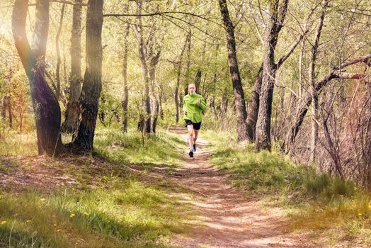 A senior man dressed in black and green is running in the forest, during a warm spring day