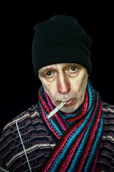 Sick man with the flu and temperature, wearing a cap and a woolen scarf, on dark background