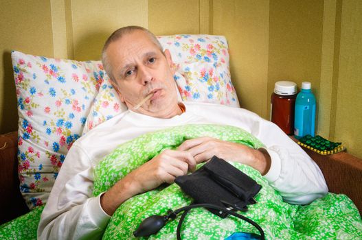 Sick man lying in bed and measuring the temperature with a thermometer