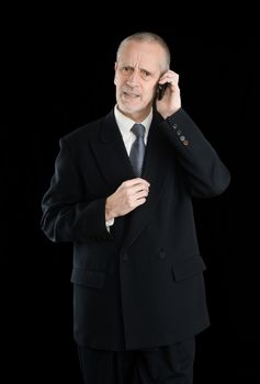 Happy businessman wearing a black suit, worried  and preoccupied on mobile phone, on black background