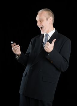 Happy businessman wearing a black suit, smiling and reading sms on mobile phone, with thumb up, on black background