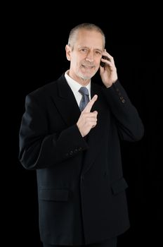 An agreeable businessman wearing a black suit smiling while speaking on mobile phone, on black background