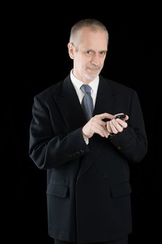 Senior businessman in black suit, writing sms or dialing a number on his mobile phone, on black background