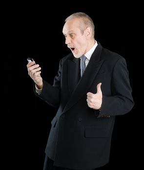 Happy businessman wearing a black suit, smiling and reading sms on mobile phone, with thumb up, on black background