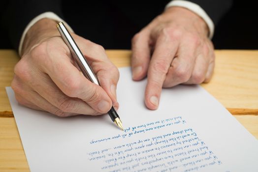 A businessman writing with a fountain pen on a white paper set on a wooded deck