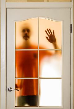 Silhouette of an unknown man in orange seen through a closed glass door, like a ghost or an alien