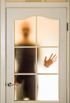 Silhouette of an unknown man in black  seen through a closed glass door, like a ghost or an alien