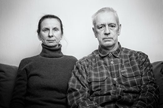 Dramatic portrait of sad and depressed adult woman and man sit on a sofa and  looking into space with lackluster eyes. Negative space for copy text