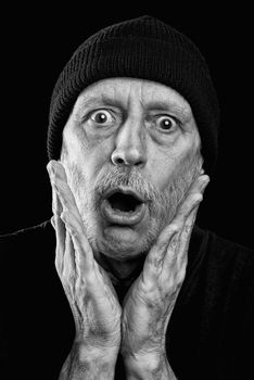 Dramatic black and white photo of a surprised or scared strong man with beard with a woolen cap on the head, putting the hands on his face