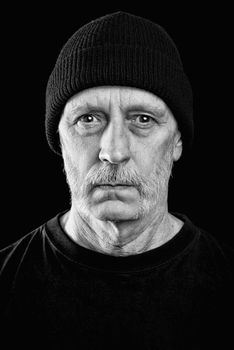 Dramatic black and white photo of a strong man with beard with a woolen cap on the head