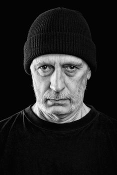 Dramatic black and white photo of a strong man with beard with a woolen cap on the head