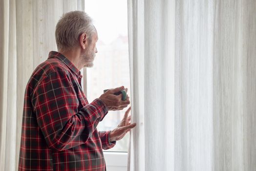 Mature man drinking his coffee in a green cup, while he is looking out of the window