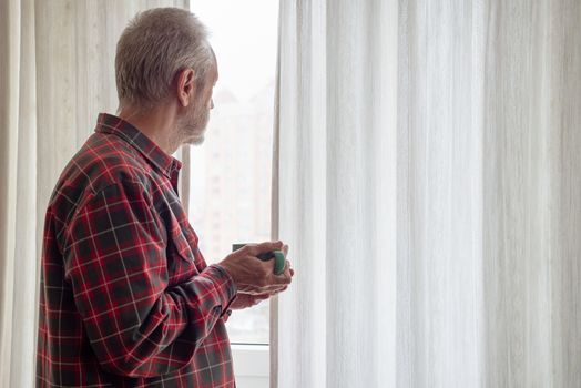 Mature man drinking his coffee in a green cup, while he is looking out of the window