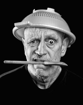 Dramatic black and white Portrait of a mad man with a mutton chops beard wearing a plastic strainer on the head and holding a wooden spoon in the mouth