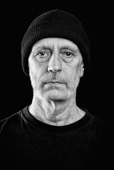 Dramatic black and white portrait of a serious and confident caucasian man with a penetrating gaze and a bit of neutral expression in the eyes, wearing a woolen cap on the head