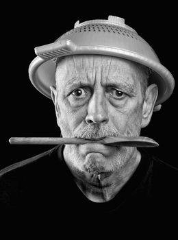 Dramatic black and white Portrait of a mad man with a plastic strainer on the head and a wooden spoon in the mouth