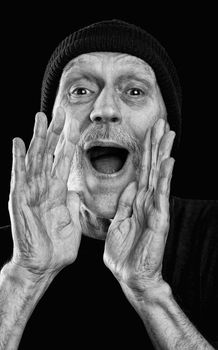 Dramatic black and white photo of a strong man with a beard with a woolen cap on the head, shouting out loud with the hands in a megaphone gesture