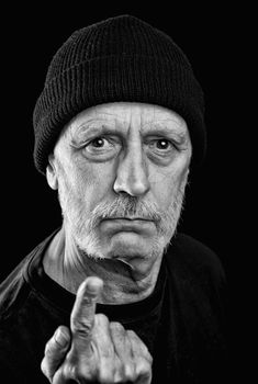 Dramatic black and white photo of a strong man with beard with a woolen cap on the head, pointing finger, with an agressive look.