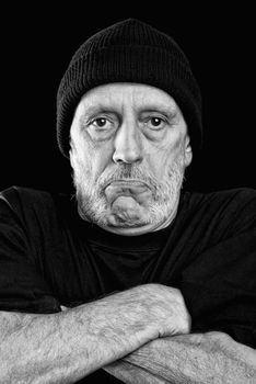 Dramatic black and white photo of a strong man with a mutton chops beard with a woolen cap on the head, crossing the arms with an agressive look.