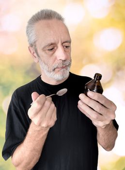 A mature man is reading the label of a cough syrup bottle before to cure his sore throat and bronchitis