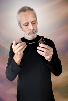 A mature man is reading the label of a cough syrup bottle before to cure his sore throat and bronchitis