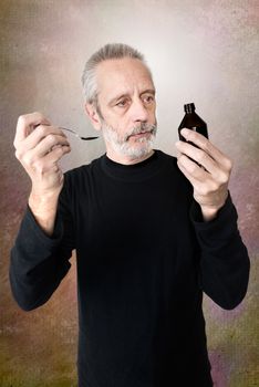 A mature man is pouring cough syrup in a spoon to cure his sore throat and bronchitis