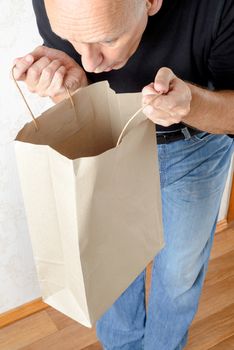 A man in blue jeans and black sweatshirt is looking inside a brown paper bag