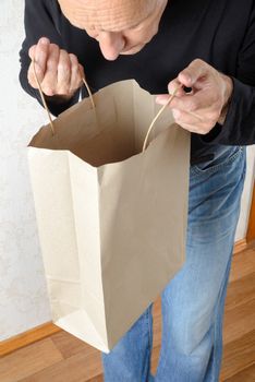 A man in blue jeans and black sweatshirt is looking inside a brown paper bag