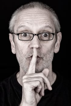 Portrait of an attractive adult man, wearing glasses, putting the finger in front of the mouth and saying "Hush!"
