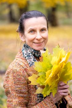 A smiling adult caucasian woman is picking yellow maple leaves in autumn in the park