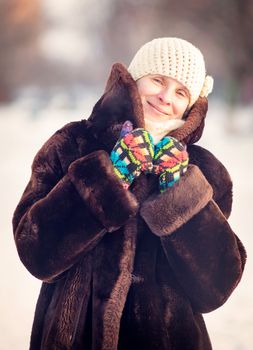 A winter portrait of a smiling senior adult woman wearing a wool cap, a scarf and colored gloves, with a snow background