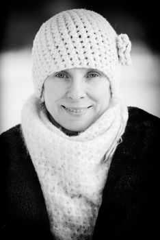 A winter portrait of a smiling senior adult woman wearing a wool cap and a scarf, with a snow background