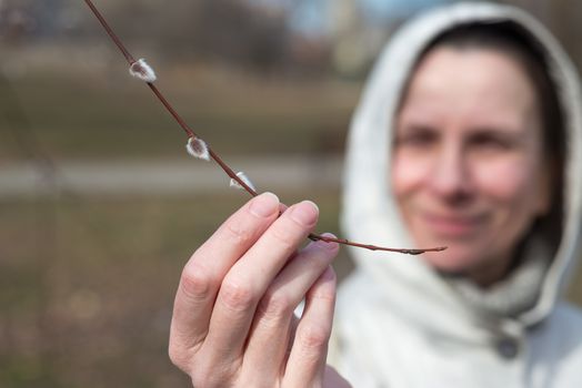 A woman is holding a willow branch in her hand and looking a catkin at the beginning of spring