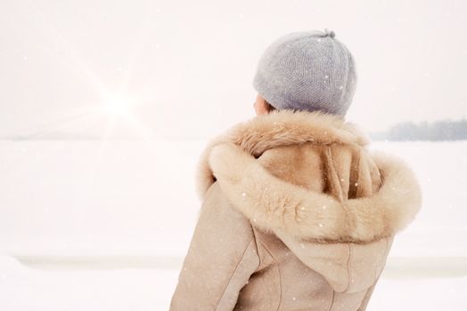 A woman with a wool cap and a leather coat is looking at the Dnieper river during a cold and magic winter morning under the snow