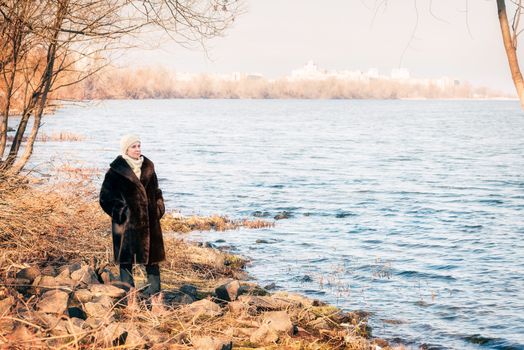 A mature woman wearing a warm fur coat and a woolen cap stays close to the Dnieper river in Kiev, Ukraine, during winter