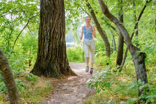 A happy senior woman is running in the forest close to the lake during a warm summer day