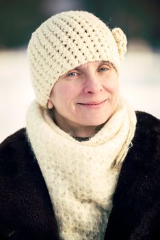 A winter portrait of a smiling senior adult woman wearing a wool cap and a scarf, with a snow background