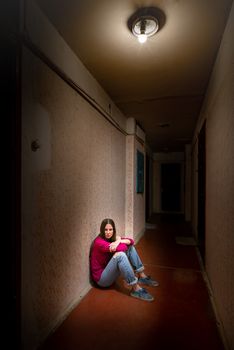 A sad and desperate woman sits in a dark corridor illuminated by a gloomy light. Her pain and her many problems pushed her into complete isolation. His sadness is only equalled by his loneliness.
