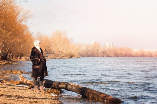 A mature woman wearing a warm fur coat and a woolen cap stays close to the Dnieper river in Kiev, Ukraine, during winter